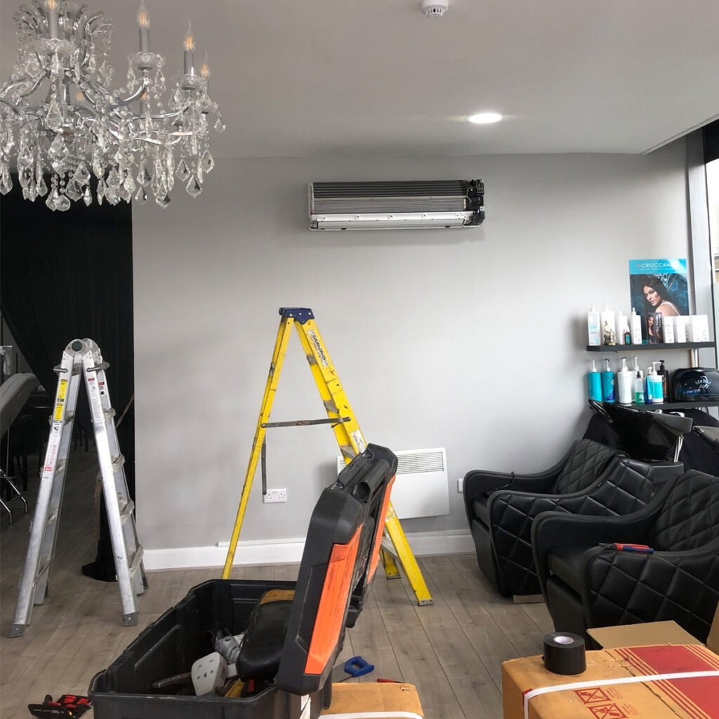 Installation or repair of a wall-mounted air conditioner in a stylish commercial setting, featuring tools, ladders, and salon chairs.